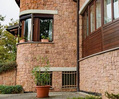 EDILIZIA RESIDENZIALE-Nuova villetta singola a Valdilana, Trivero (BI) - 1995
Questo edificio, collocato in posizione dominante in cima a una collina, ha una disposizione in pianta con una forma leggermente arcuata, in modo da privilegiare la facciata sud, dove la vista e l'esposizione sono migliori. Abbiamo realizzato la struttura in cemento armato seguendo le particolari forme della pianta dell'edificio, mentre abbiamo eseguito il rivestimento esterno con  blocchetti squadrati a mano di porfido rosso proveniente dalle cave di Cuasso al Monte (VA). A nostro avviso tutto questo ha reso l’effetto finale molto particolare. Infine, nel piano giorno è presente il giardino interno che si affaccia per mezzo di vetrate sui locali interni e prende la luce naturale dall'alto. 
